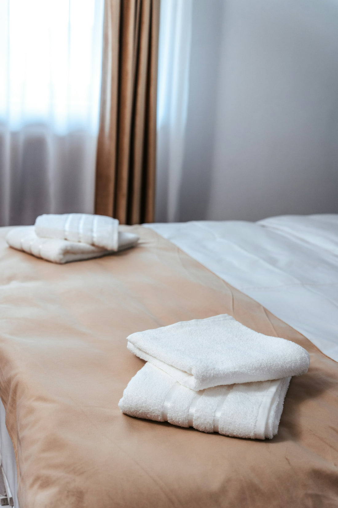 Neatly folded white bath towels on a neutral bed